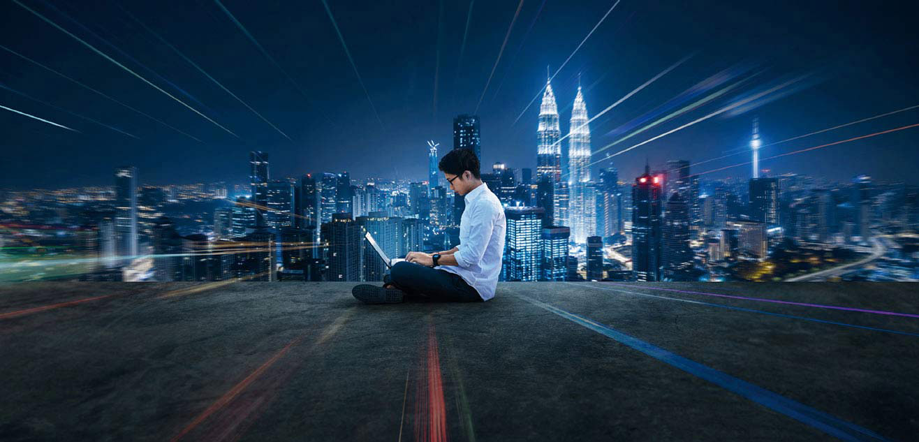 A man sitting on the floor using laptop with Malaysia night view